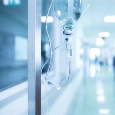 A photo showing an antibiotic drip on a stand in the foreground, with the corridor of a hospital in the blurred background. 